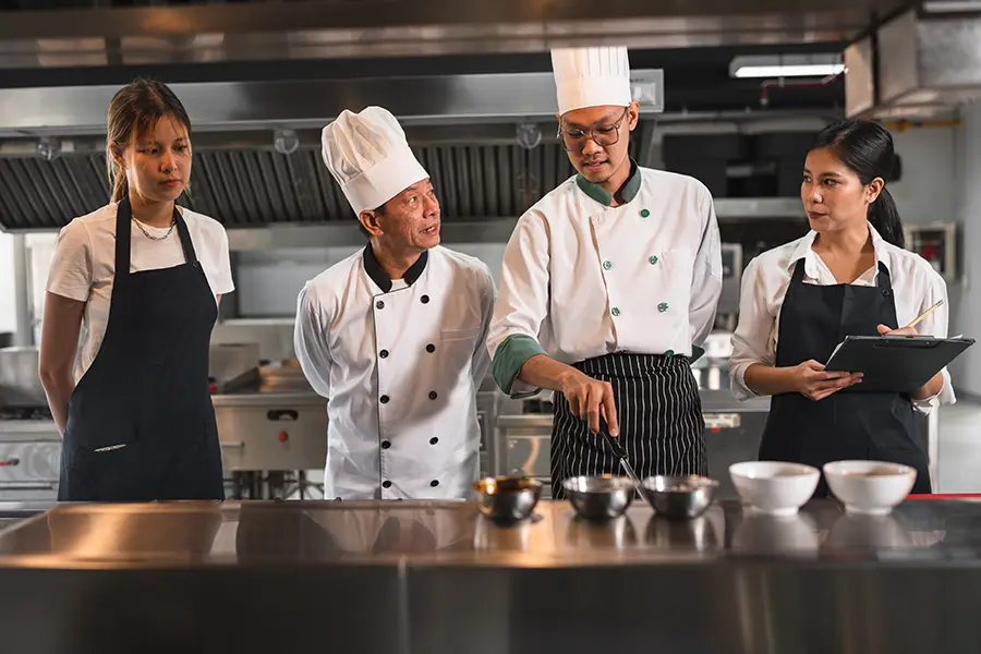 Executive Chef กำลังยืนควบคุมทีมงานในครัวอย่างมั่นใจ สะท้อนความเป็นผู้นำ